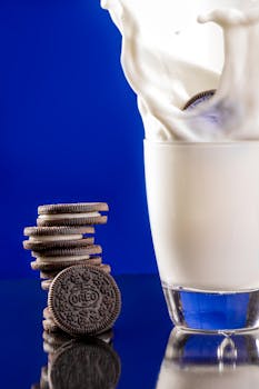 A stack of chocolate cookies next to a glass of milk with a splash against a blue background.