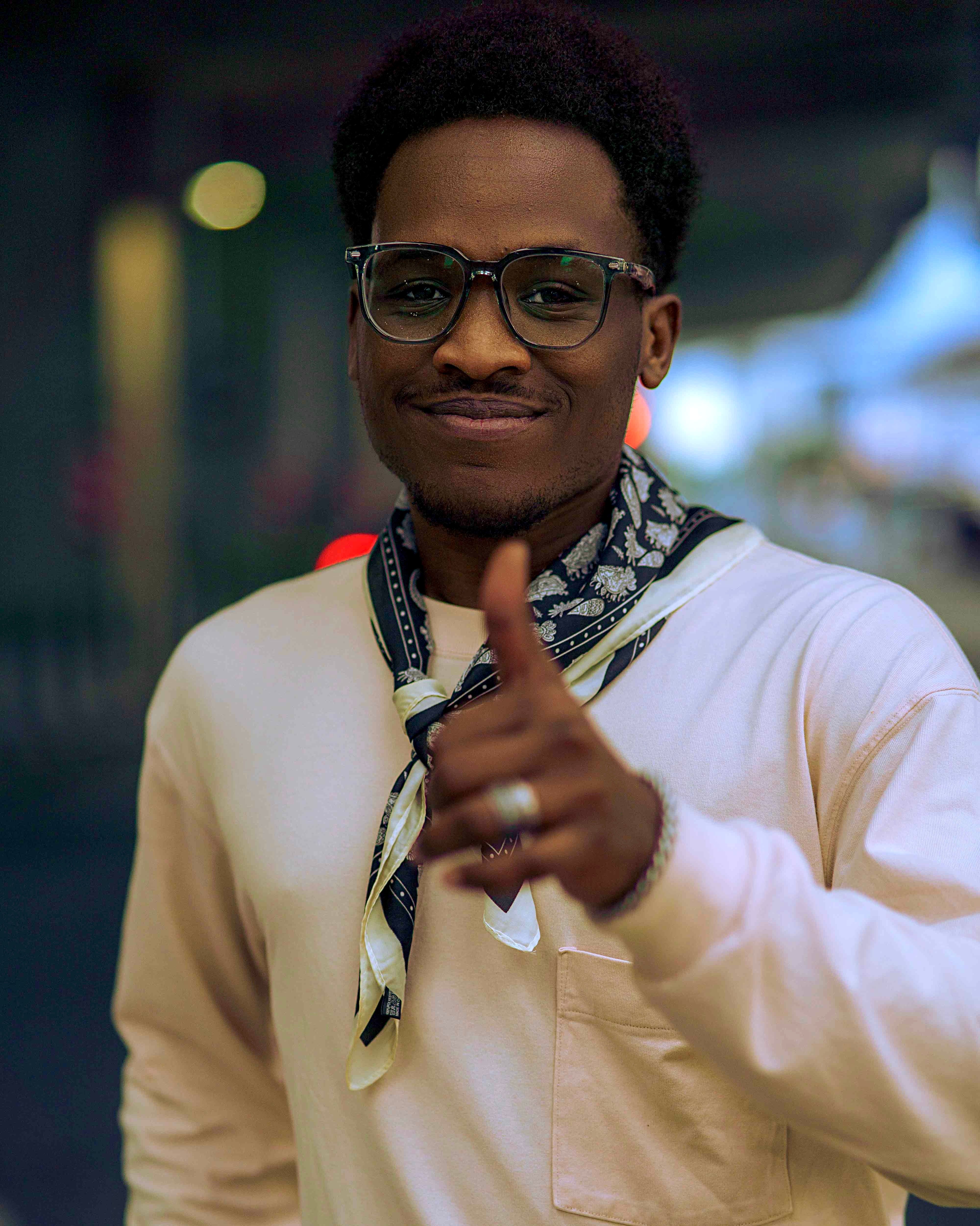 Confident man wearing glasses giving a thumbs-up in an urban setting.