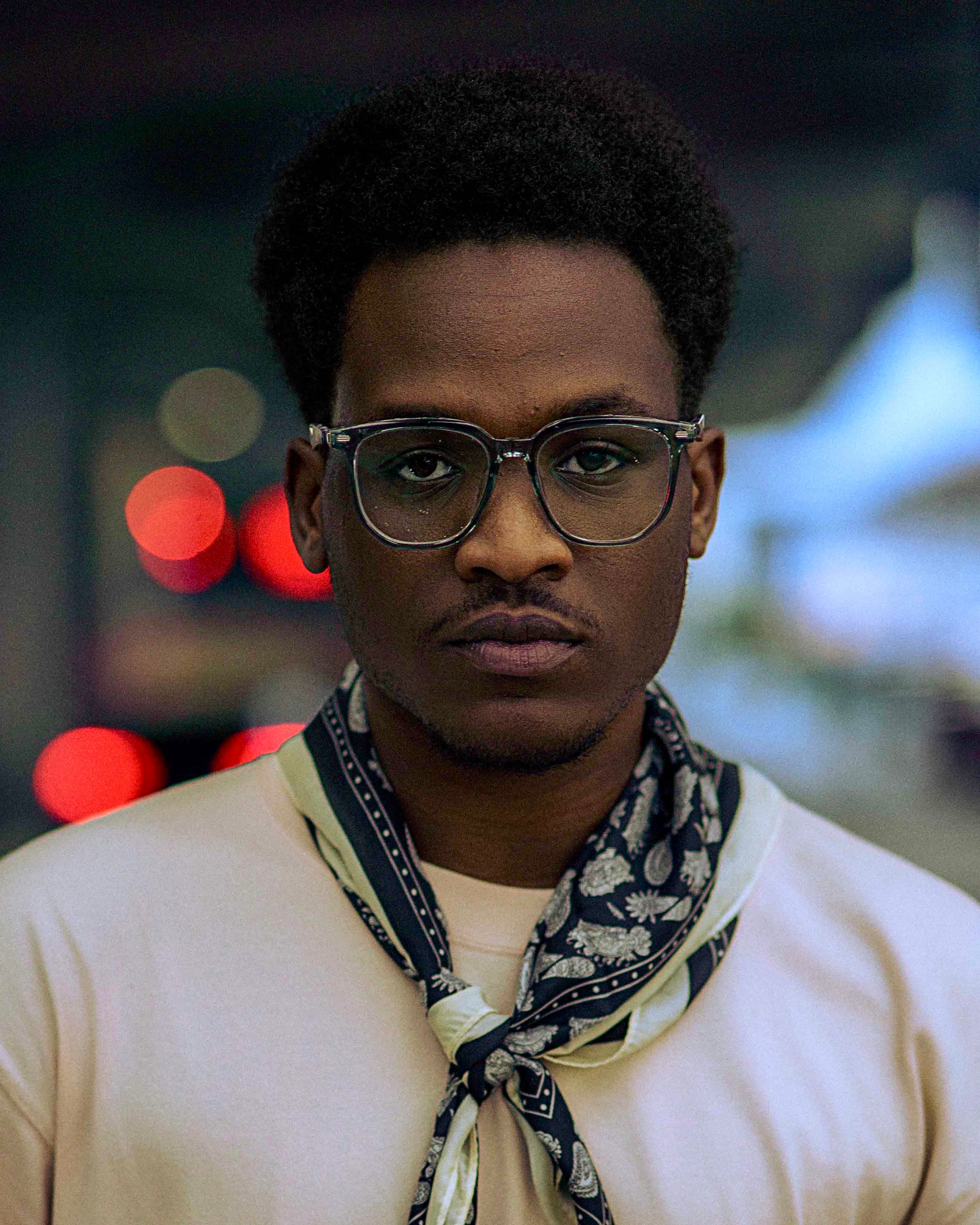 Close-up portrait of a young man wearing glasses and a scarf at night.
