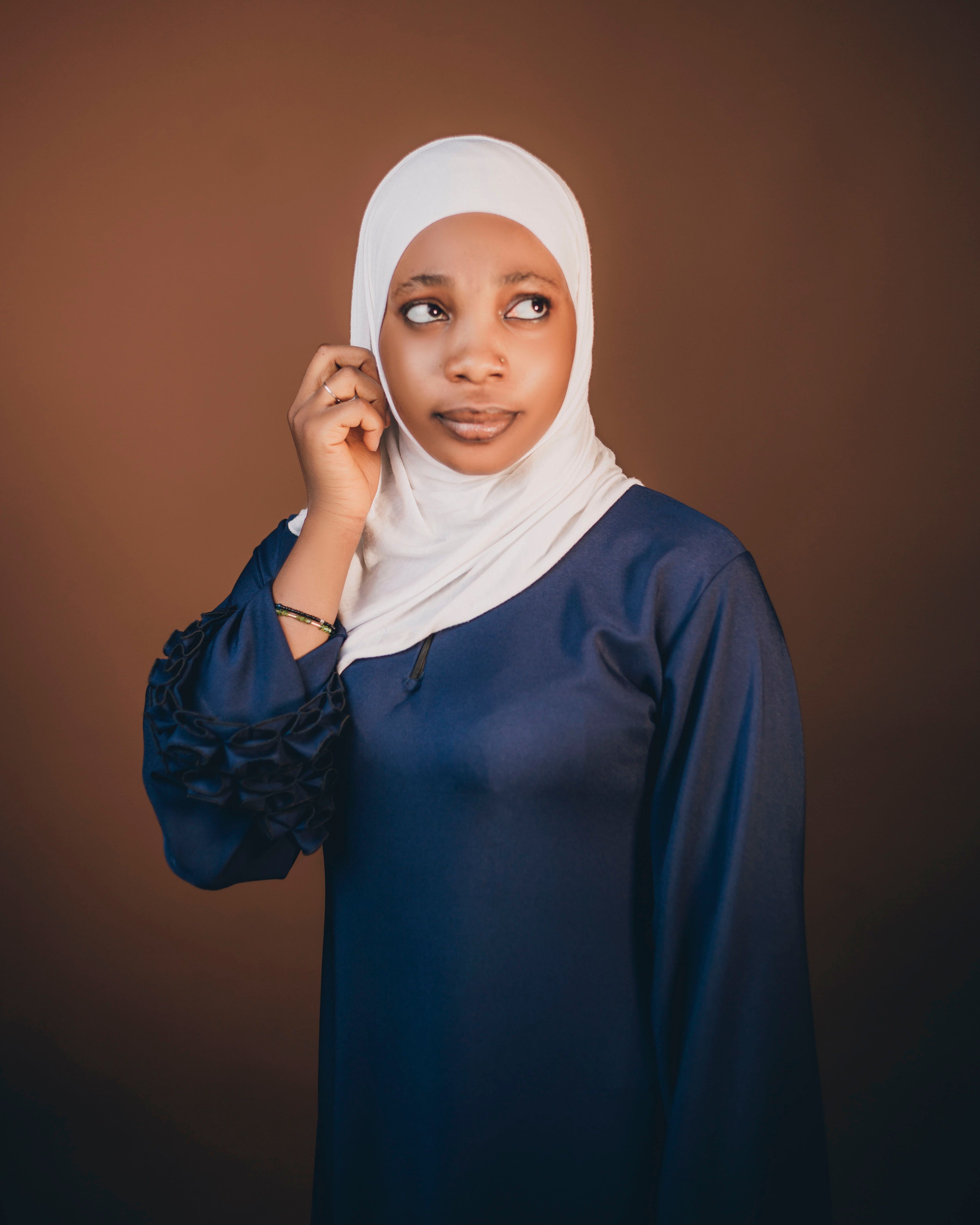 Thoughtful Young Woman in Hijab Against Brown Background · Free Stock Photo