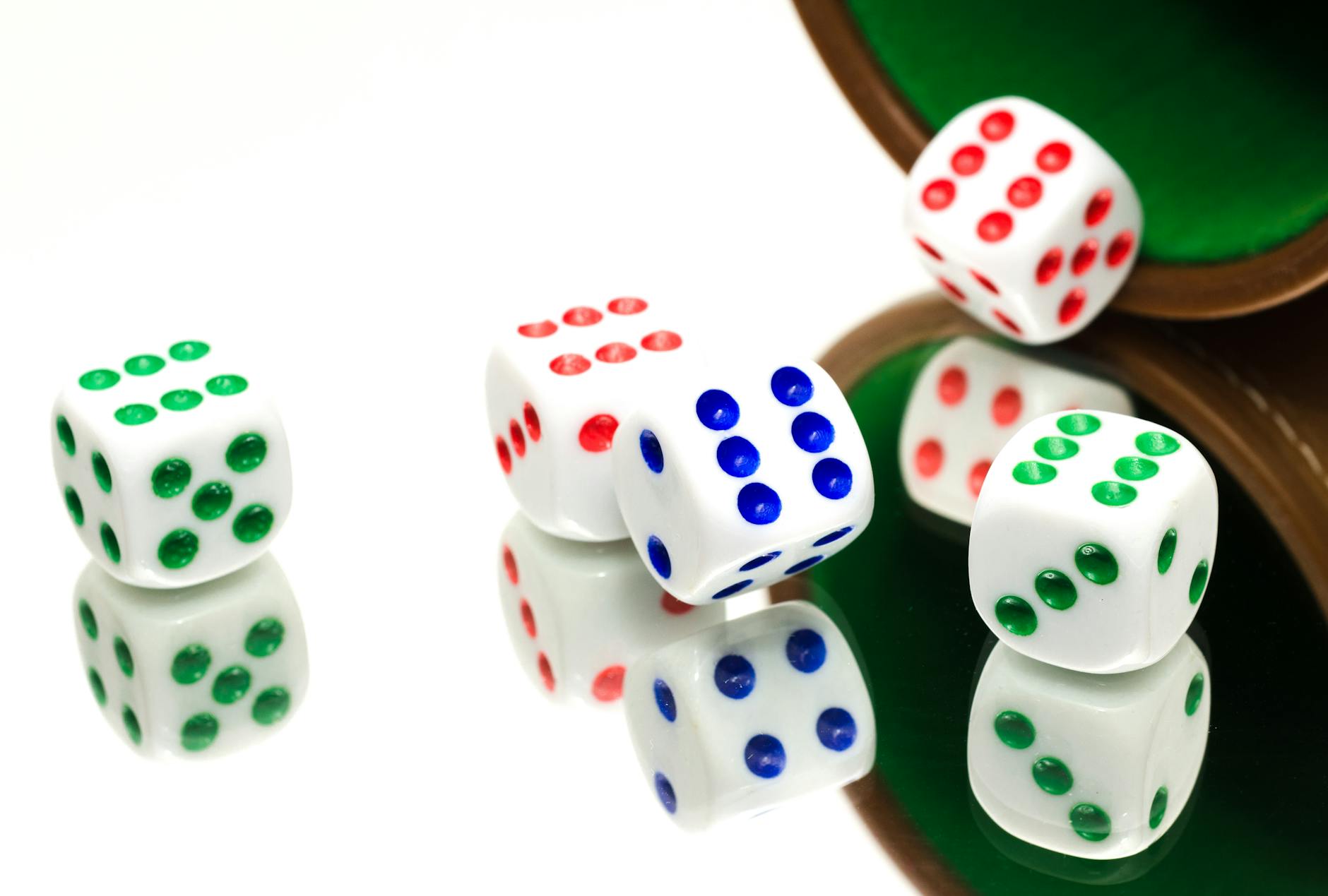 White dice with colorful dots scattered on a reflective surface, evoking gaming and chance.