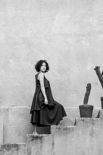 Black and white photo of a stylish woman on stairs in a minimalist setting.