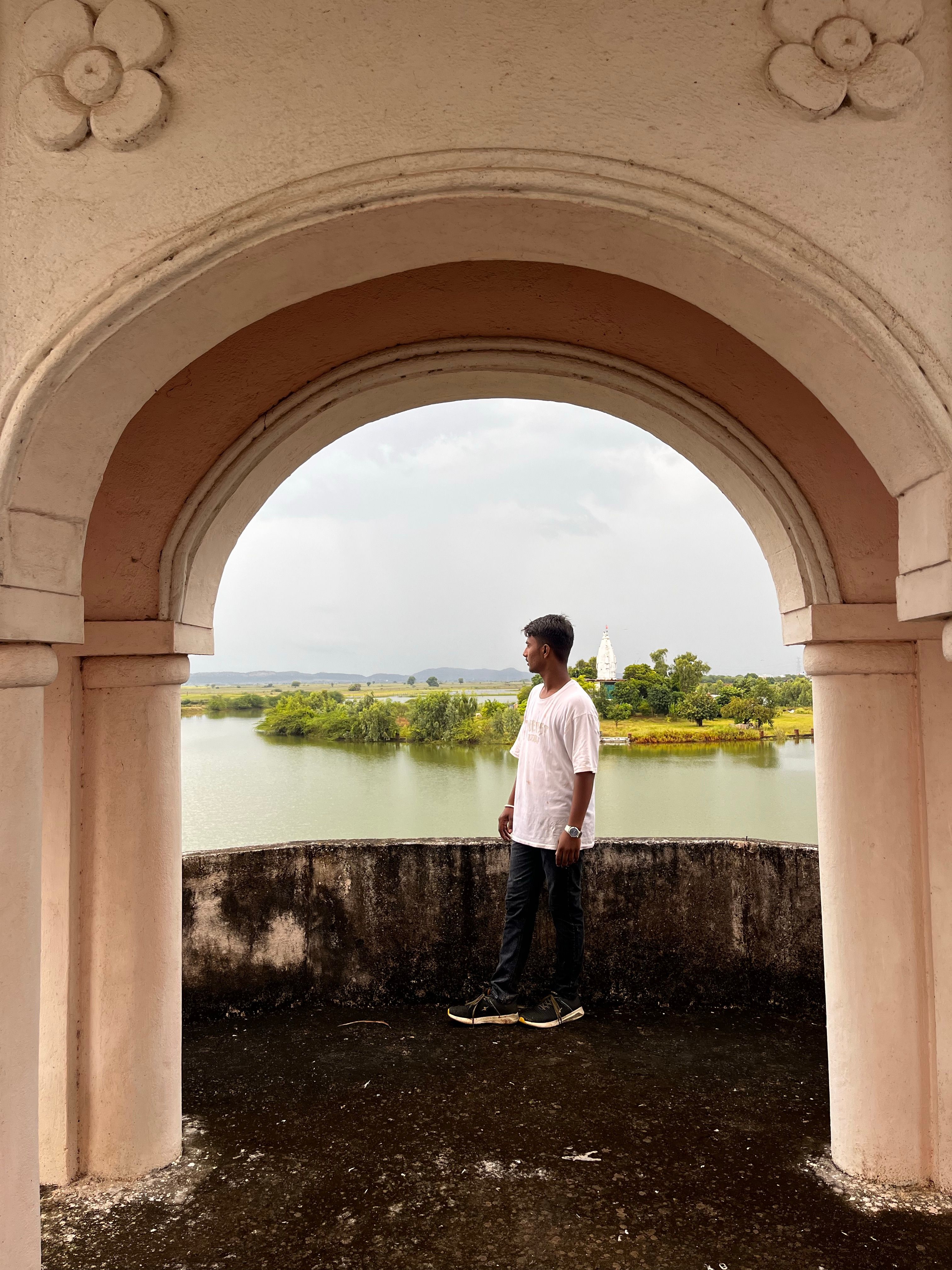 A man stands by a scenic river view framed by an archway, reflecting a tranquil outdoor scene.