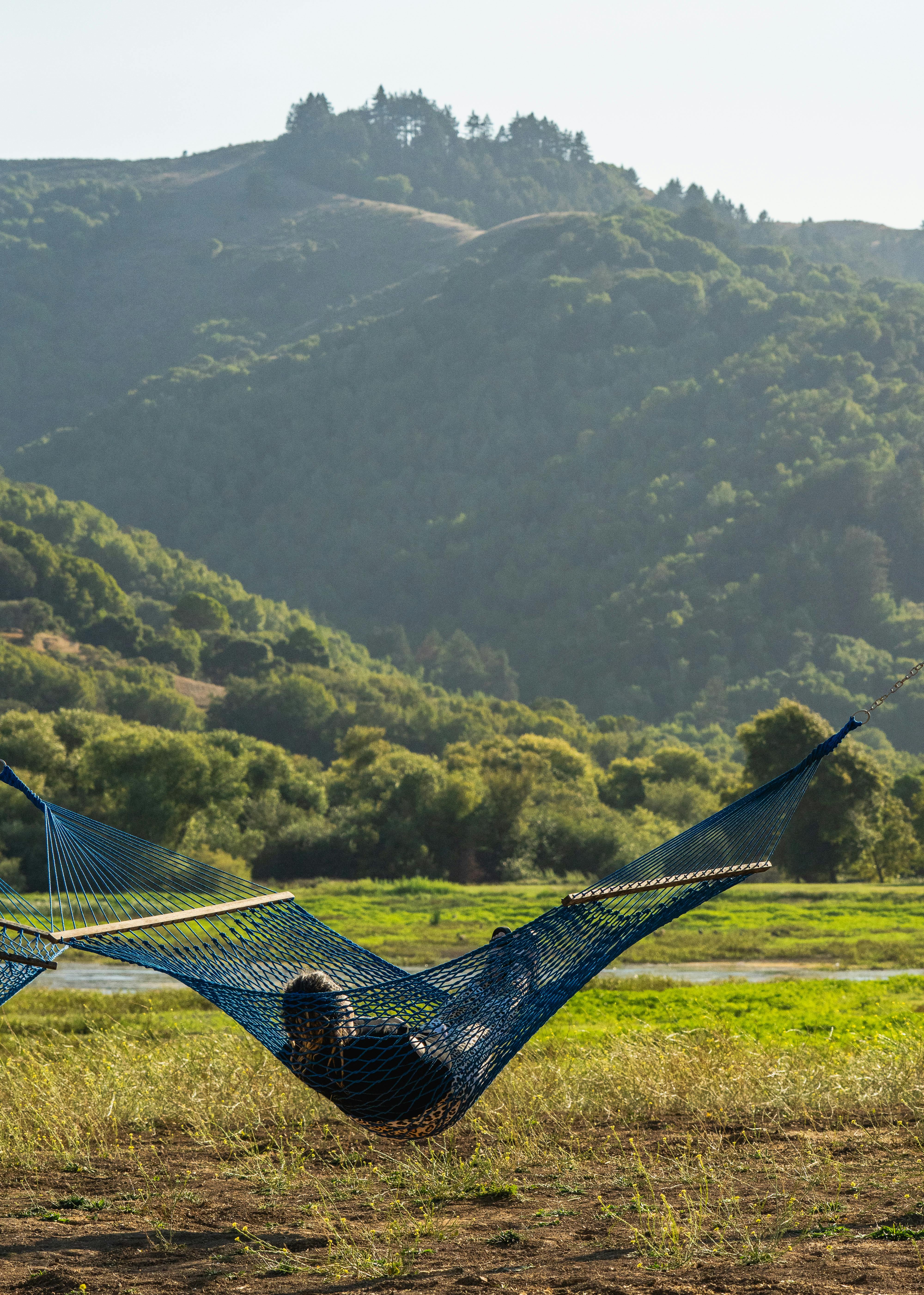 Person relaxing in a hammock with a stunning view of green mountains and clear skies.