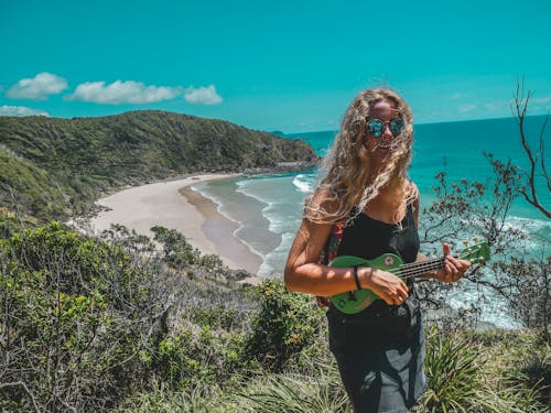 Free Woman Standing on Mountain While Playing Guitar Near Seashore Stock Photo