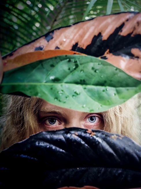 An artistic peek-a-boo portrait with vibrant jungle leaves.