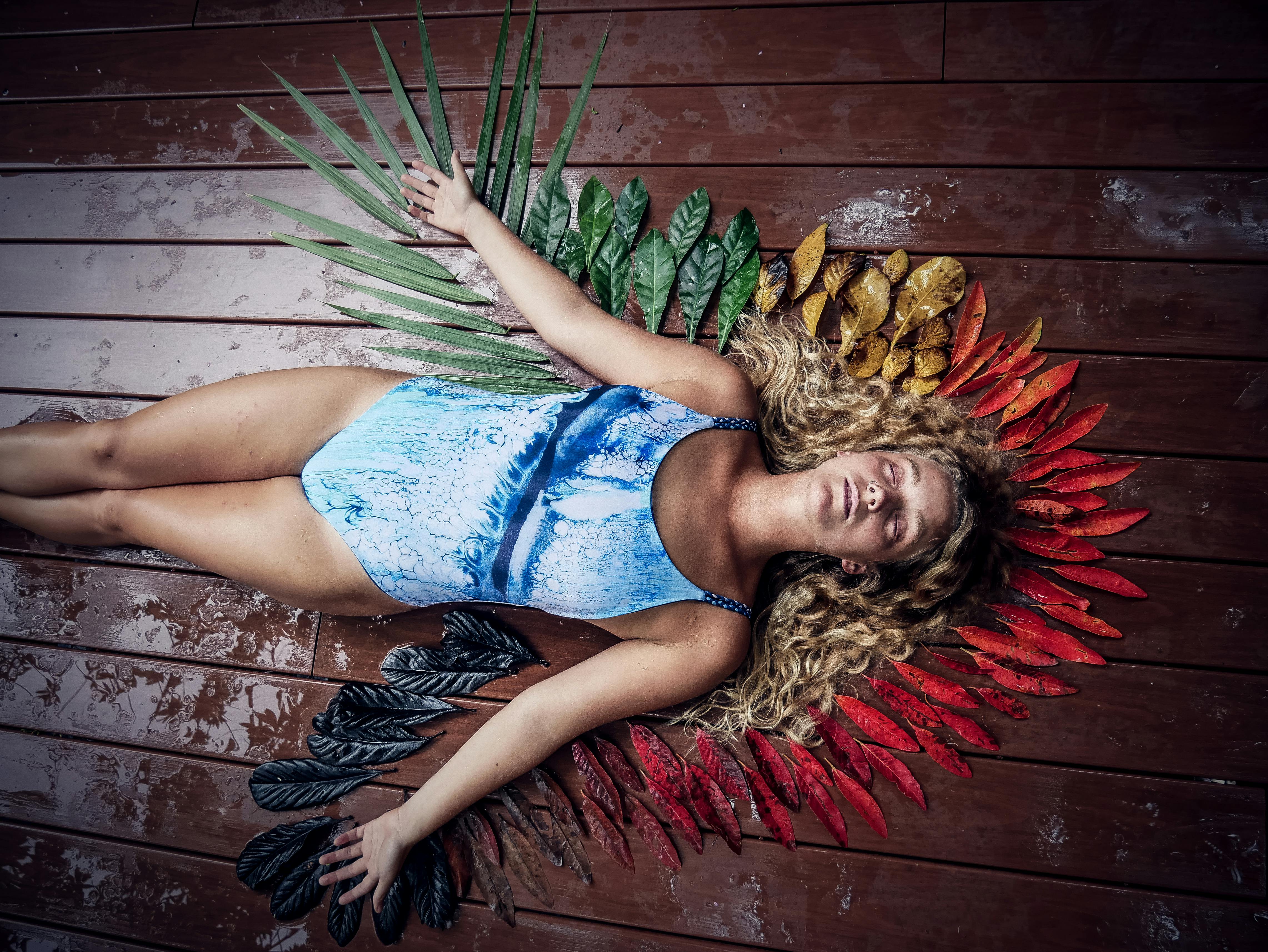 一名身穿蓝色泳衣的女子躺在木甲板上，四周环绕着鲜艳的树叶