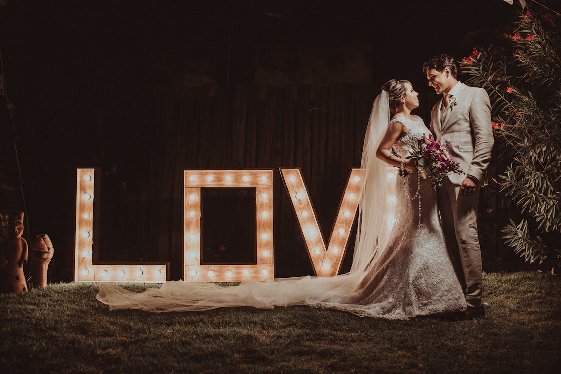 Groom and Bride Standing Beside a Love Marque Light Signage