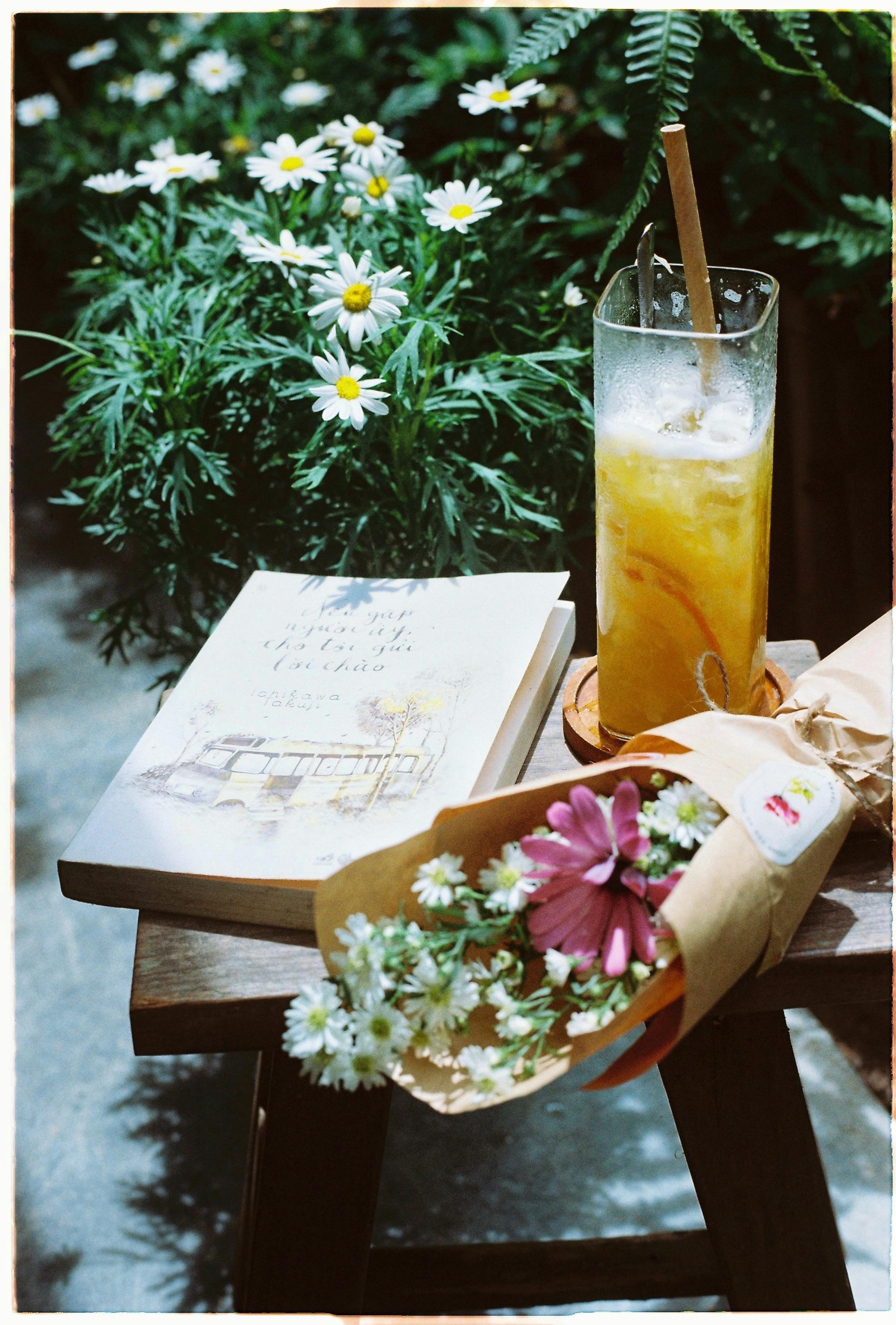 A cozy scene with a book, flowers, and iced drink on a sunny day.