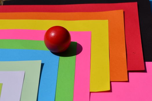 Vibrant layered colored papers with a red ball on top creating a striking visual contrast.
