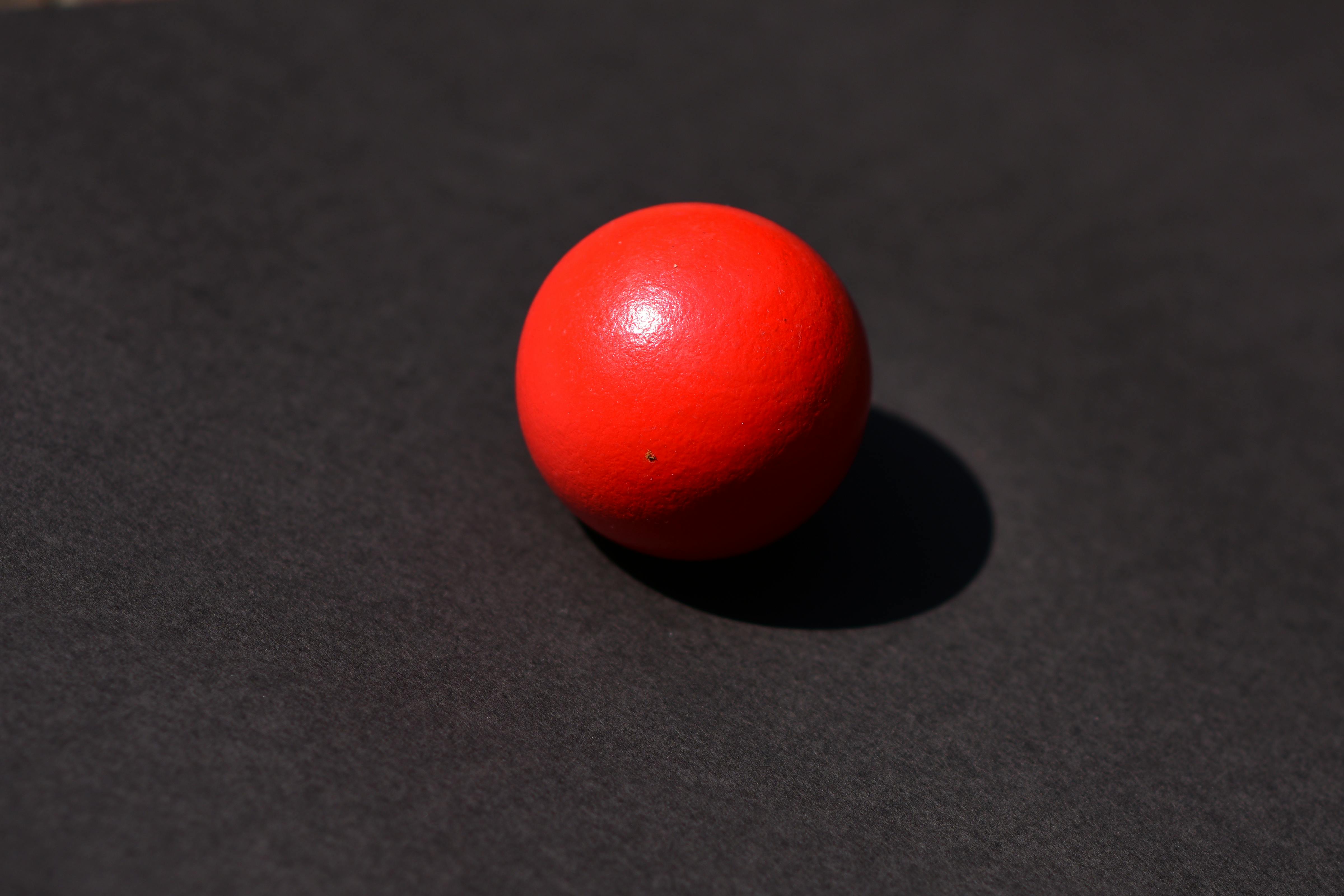 Gratuit Une boule rouge vibrante projetant une ombre sur un fond sombre, capturant un design minimaliste. Photos