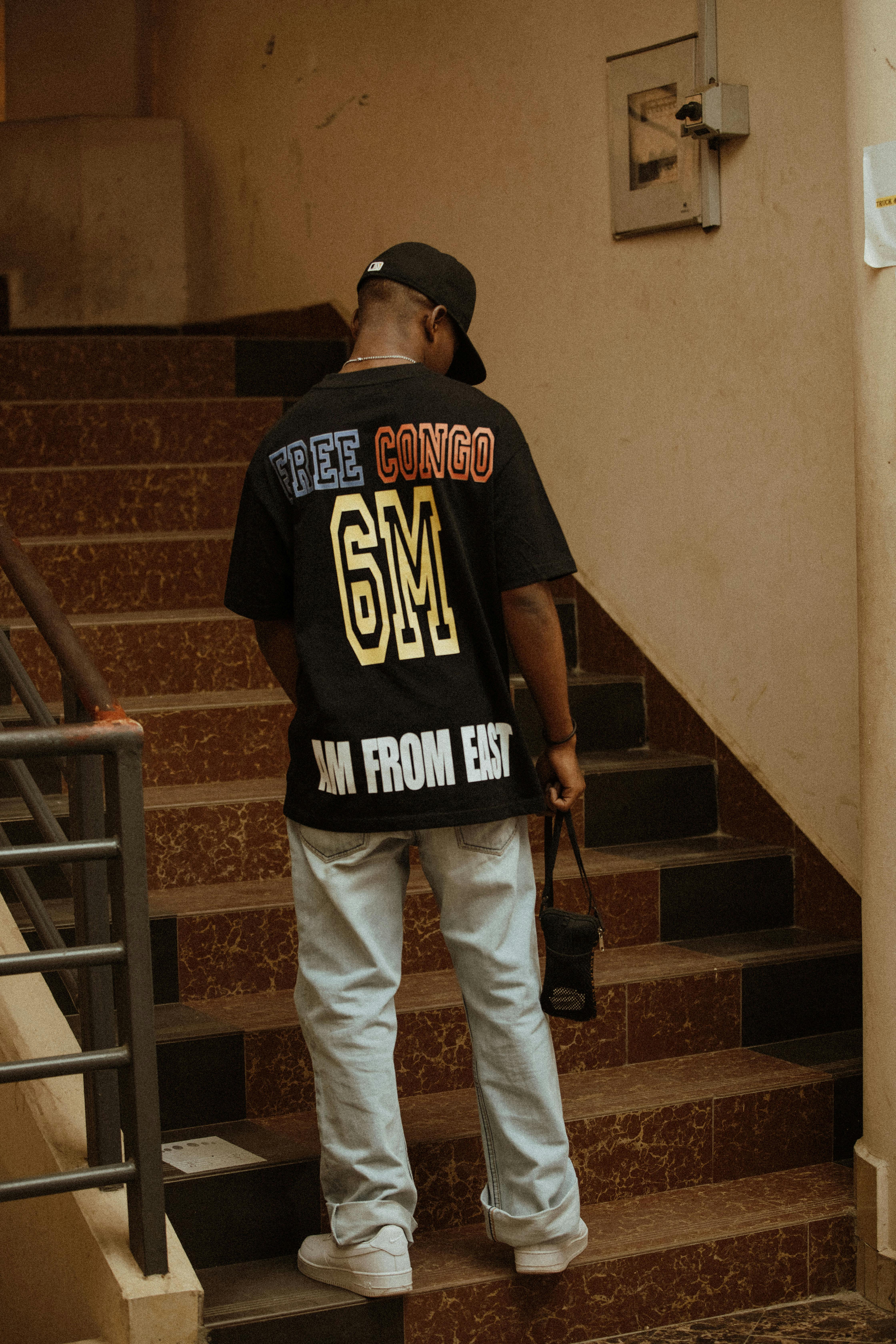 A young man stands on a staircase wearing a shirt with a bold text message.