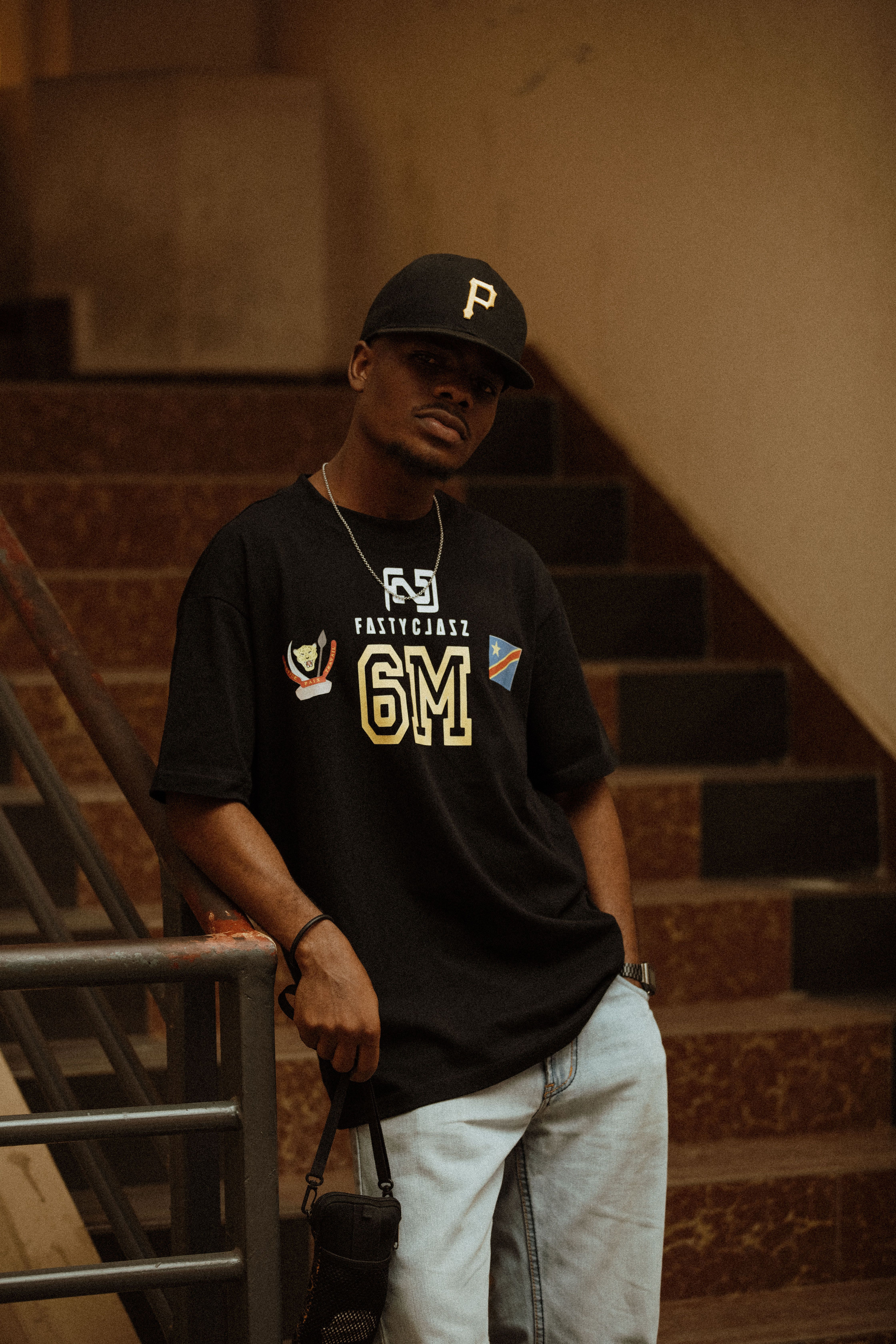Stylish man in casual attire posing on a staircase, showcasing urban fashion.