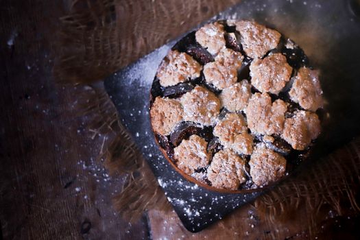 A rustic fig tart with a crumbly topping dusted with powdered sugar on a wooden table.