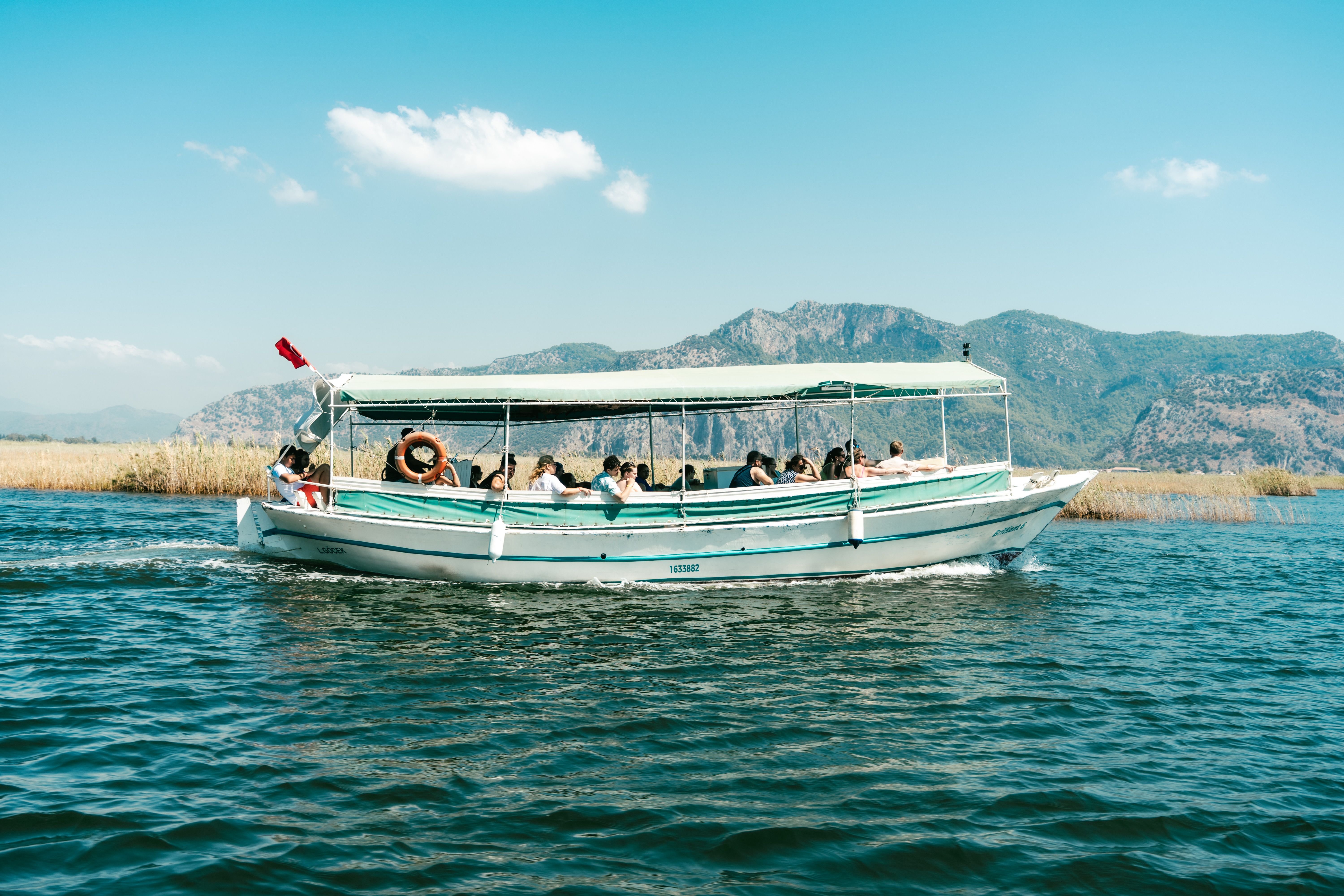 Boat cruising on serene lake with passengers enjoying mountain views under clear skies.