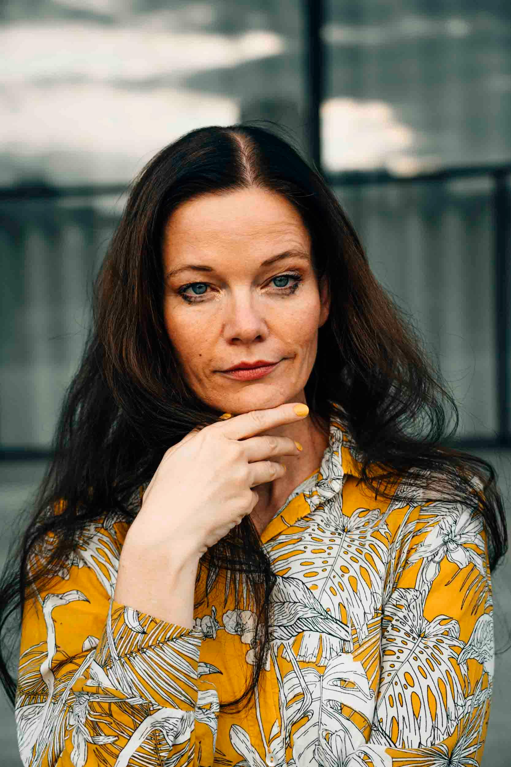 A thoughtful woman in a yellow patterned shirt photographed outdoors in Berlin.