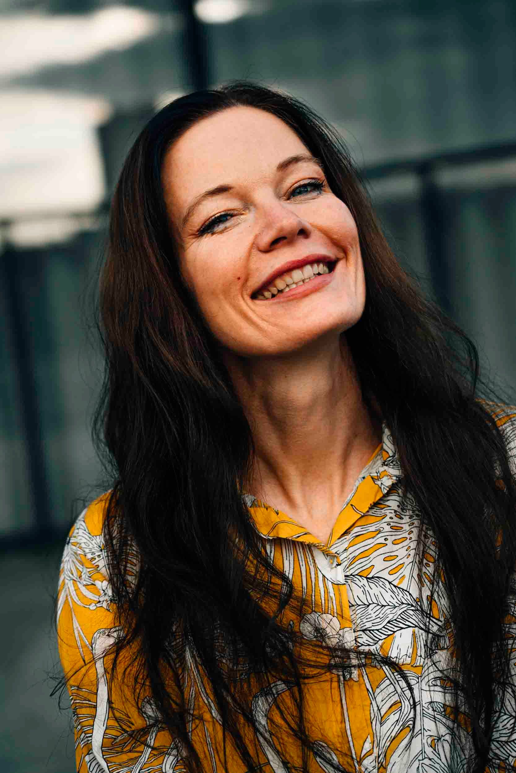 Candid portrait of an adult woman smiling, wearing a yellow shirt, outdoors in Berlin.