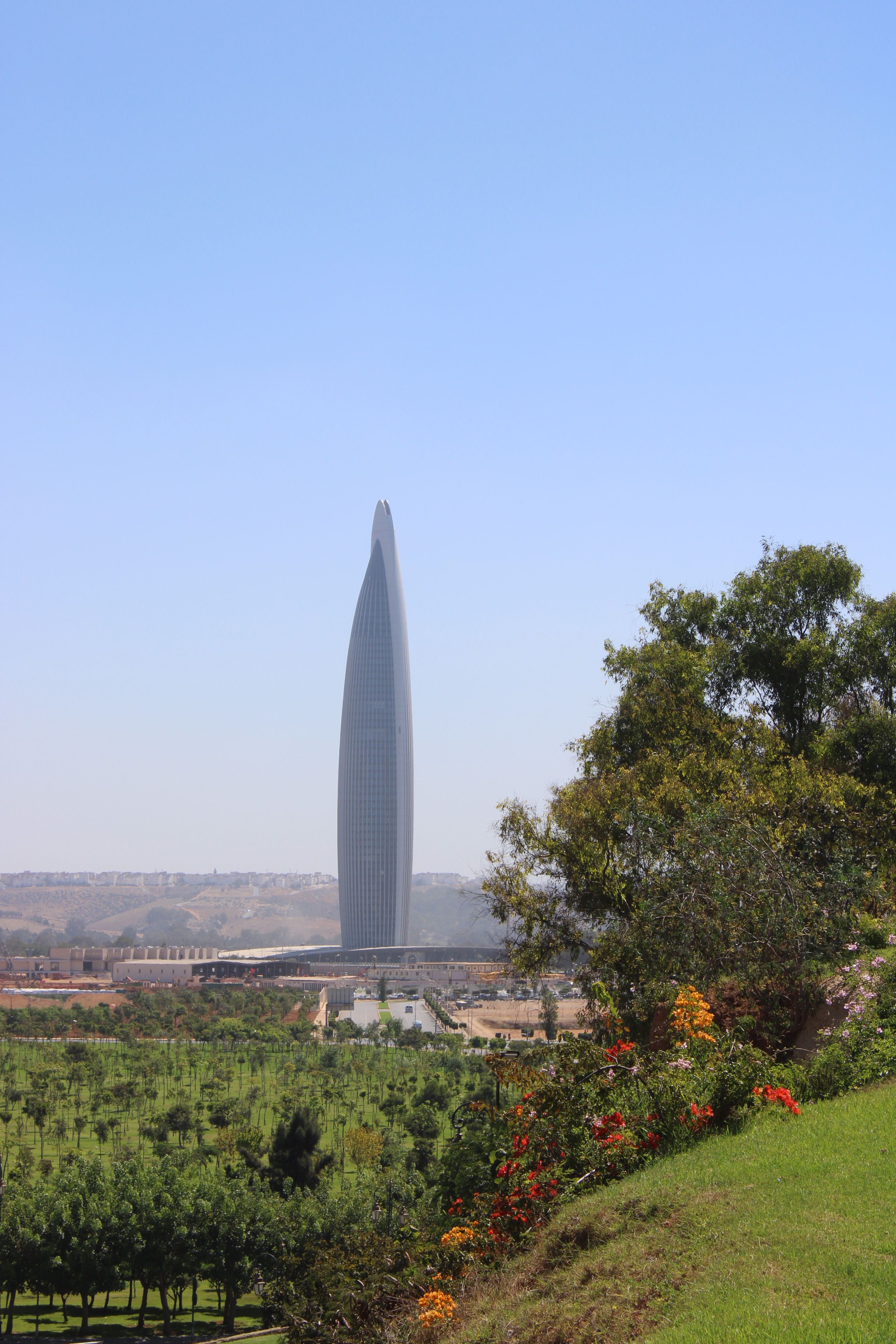 View of an iconic tall skyscraper in Rabat, Morocco amidst greenery and blue sky.