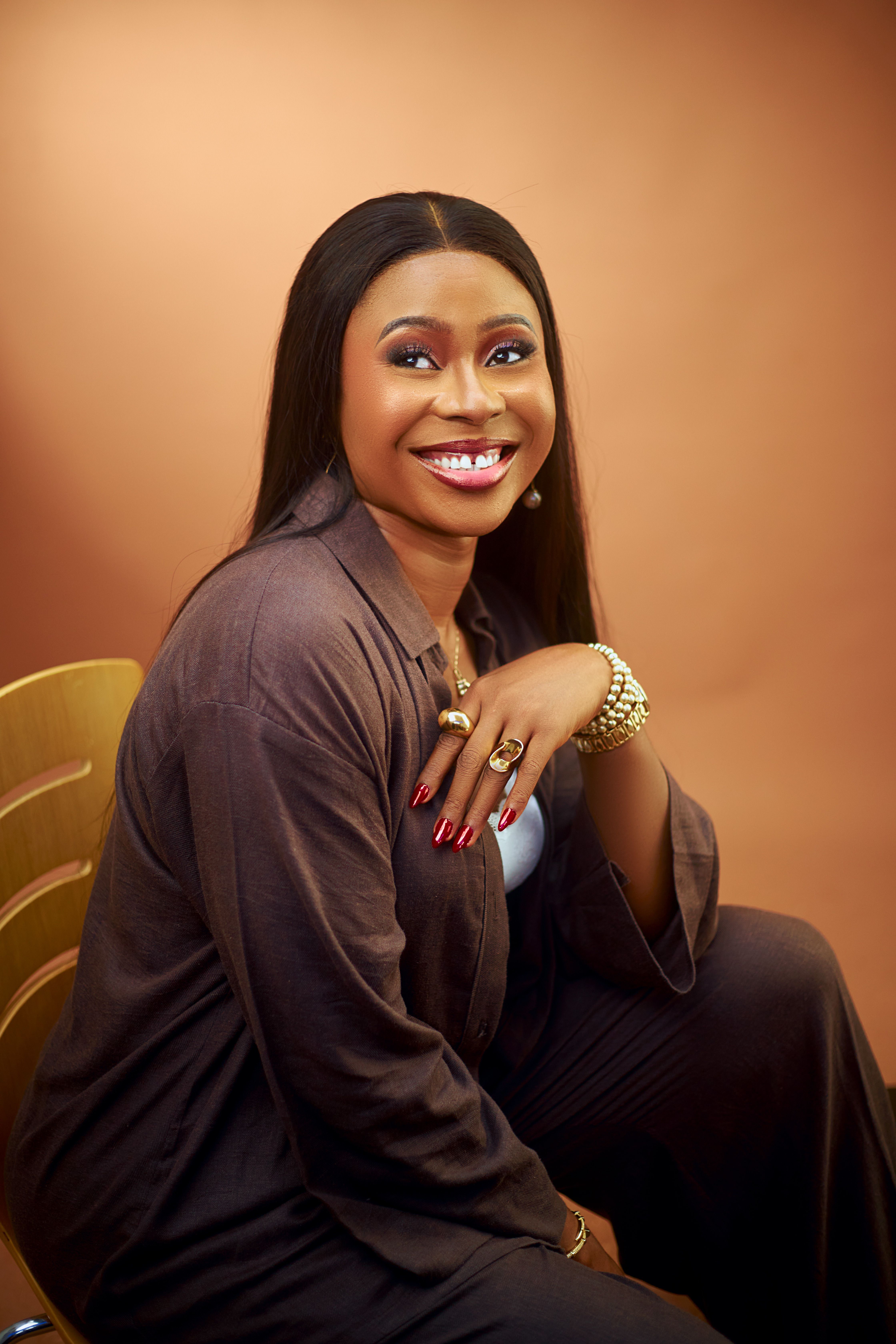 Sophisticated woman in elegant outfit smiling, seated indoors. Warm tones, chic style.