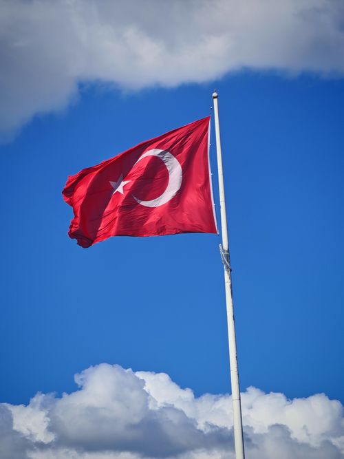 Free Turkish national flag with crescent and star waving under a vibrant blue sky with clouds. Stock Photo