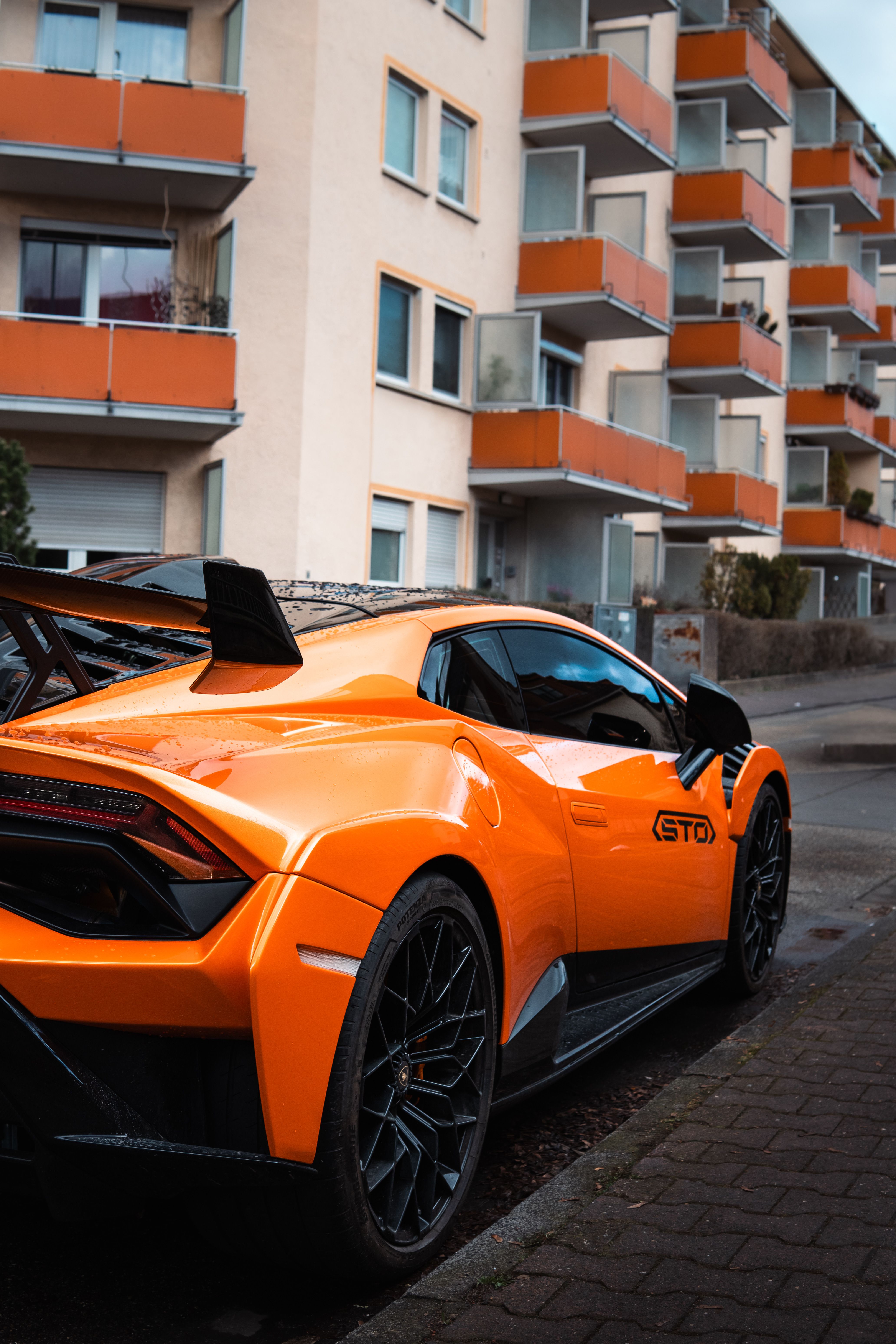Bright orange Lamborghini Huracan STO parked on urban street with modern apartments in background.