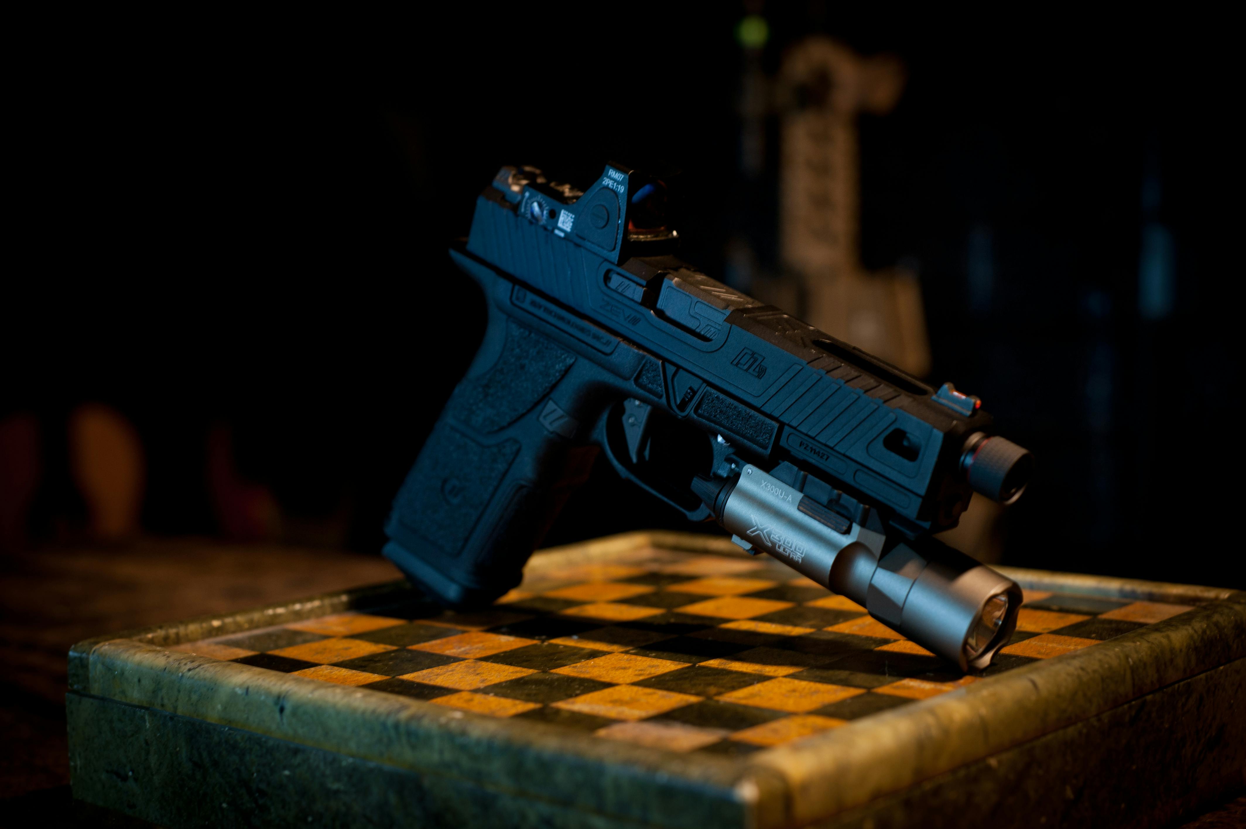 A detailed black handgun on an ornate wooden board with a dark background.