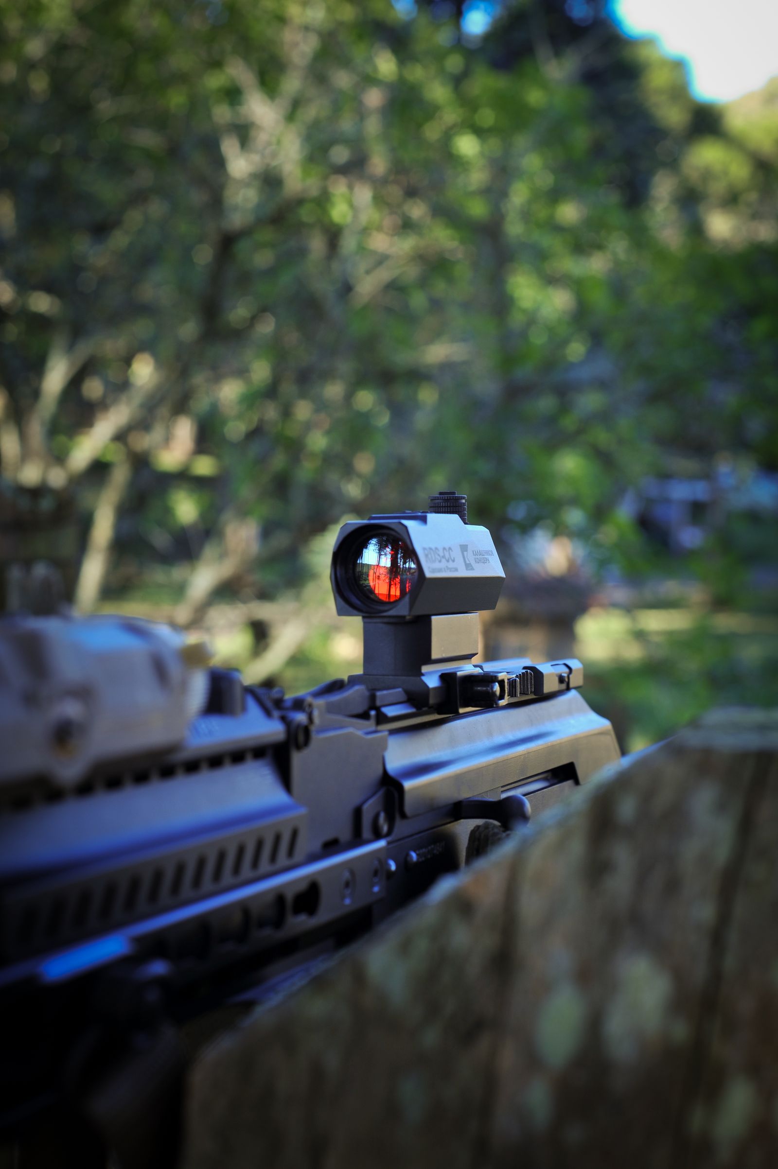 Tactical rifle equipped with a red dot sight outdoors, representing solar and battery-powered optic options