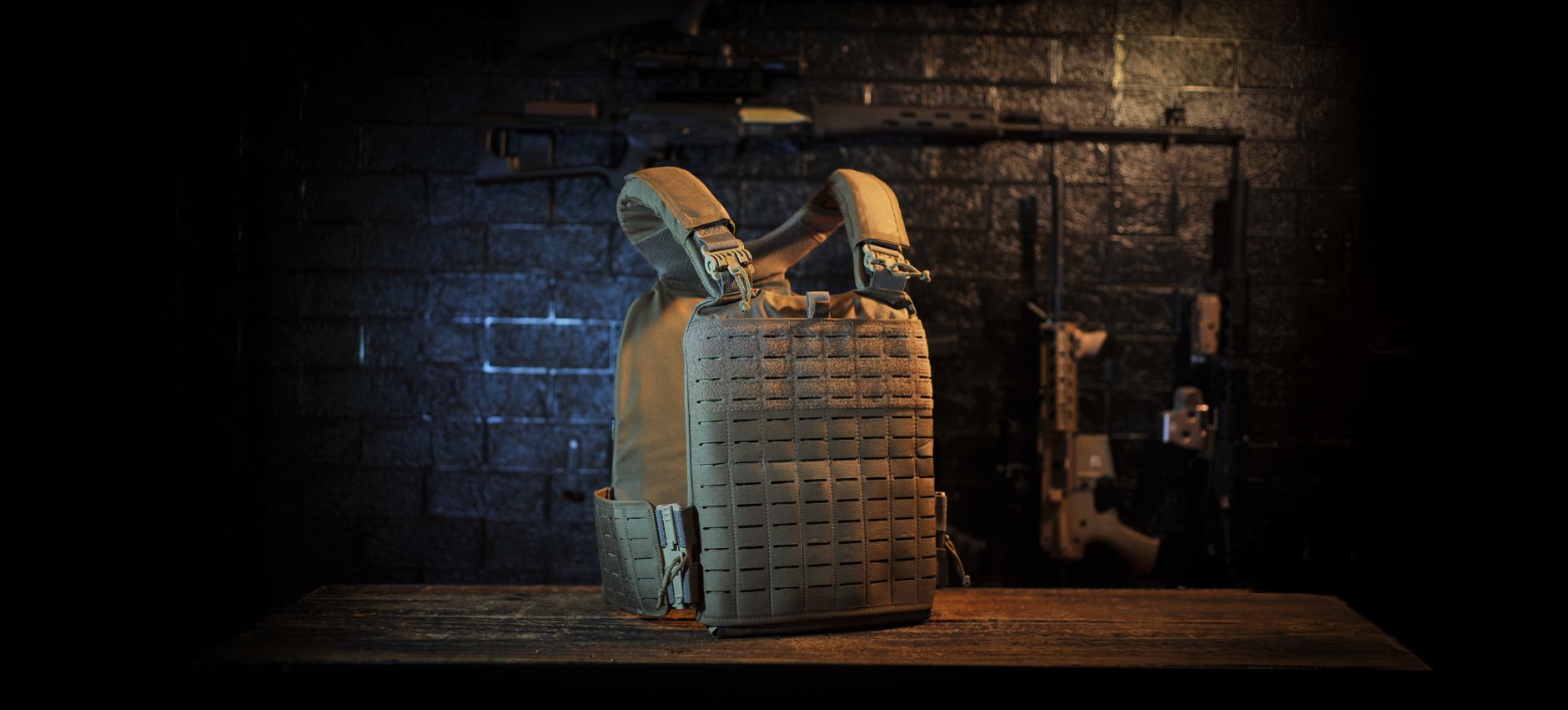A tactical vest displayed in an armory setting with rifles on a wall.