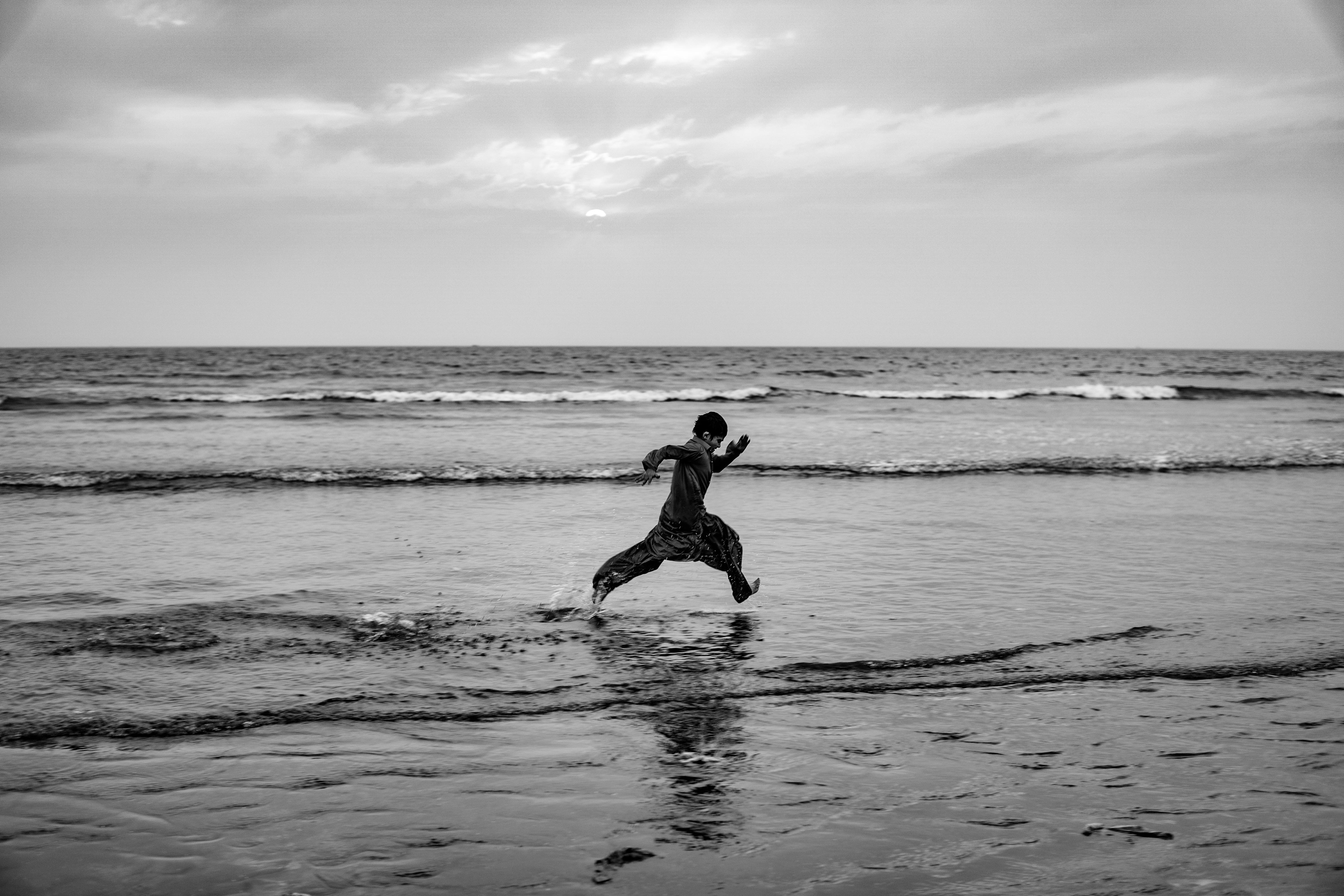 A person leaps energetically along a serene beach, captured in monochrome.