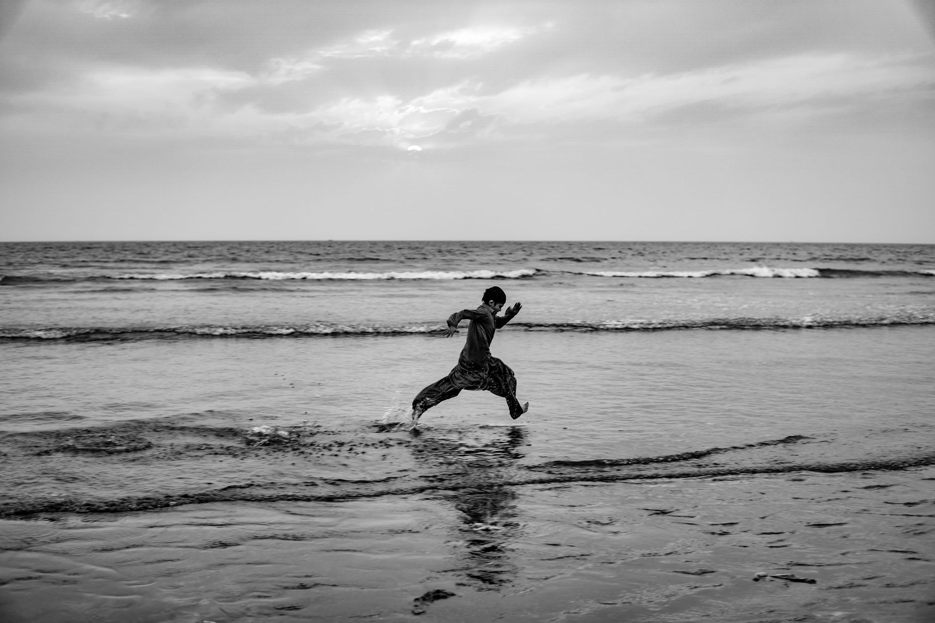 A person leaps energetically along a serene beach, captured in monochrome.