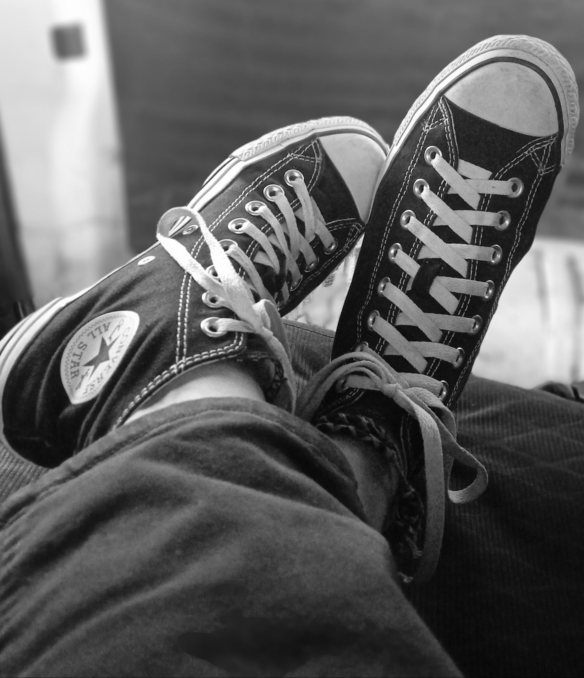 Black high top canvas sneakers worn indoors, captured in monochrome, showcasing a relaxed lifestyle.