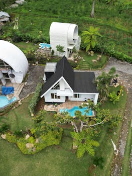 Aerial view of a modern tiny house with pool set in a lush green landscape.