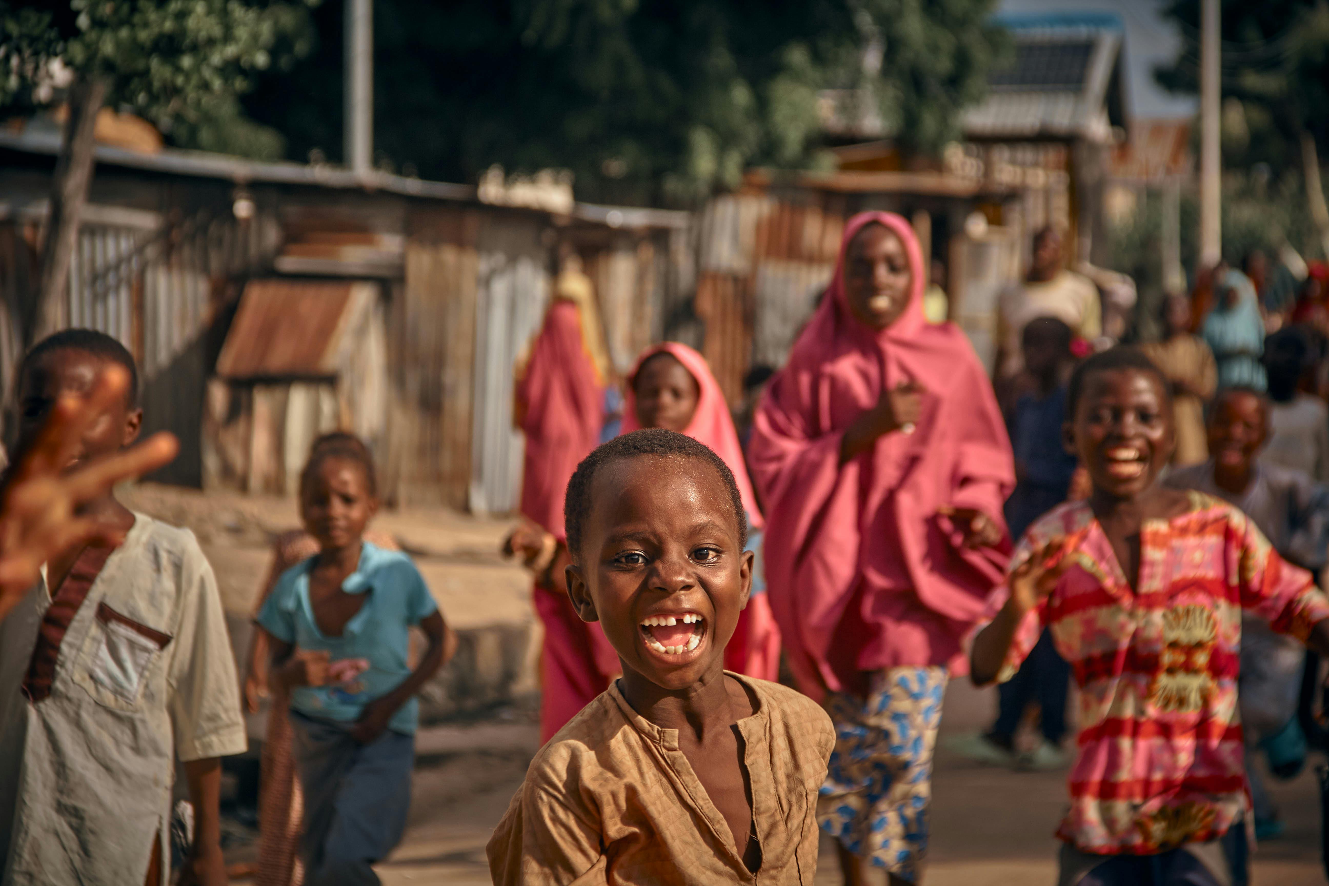 Children laughing and playing in a vibrant African village street scene, full of energy.