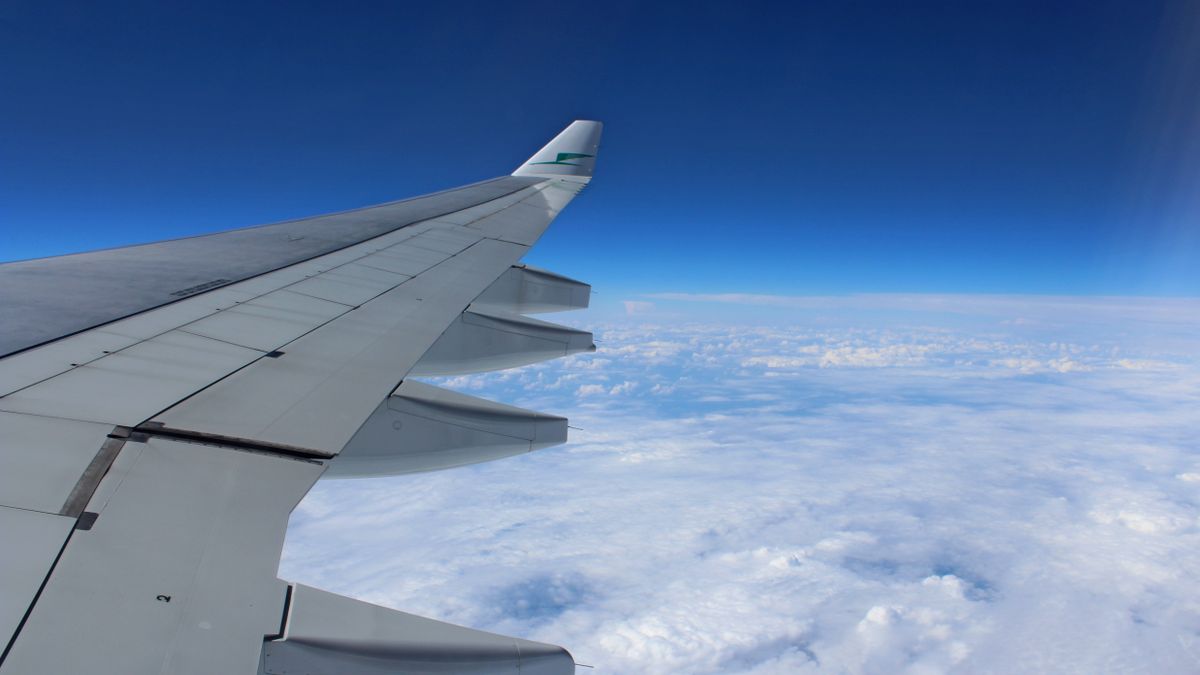 View of airplane wing in flight over cloudscape with clear blue sky.