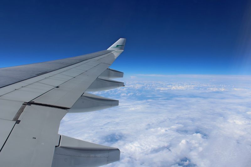 View of airplane wing in flight over cloudscape with clear blue sky.
