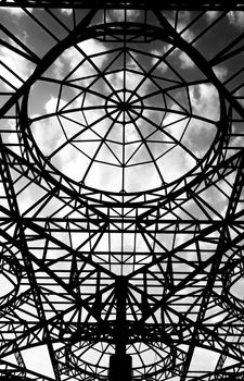 Black and white abstract view of a steel structure canopy with cloudy sky.