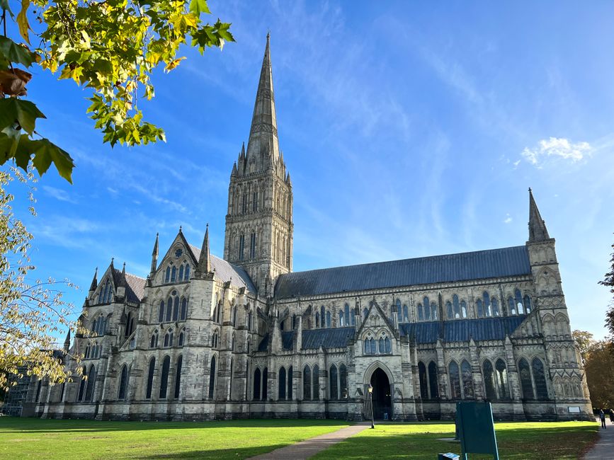 Salisbury Cathedral under a clear blue sky, showcasing Gothic architecture and a sprawling green lawn.
