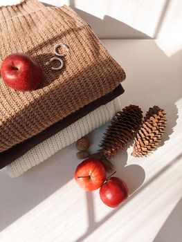 Cozy autumn setup with sweaters, apples, and pine cones in sunlight.