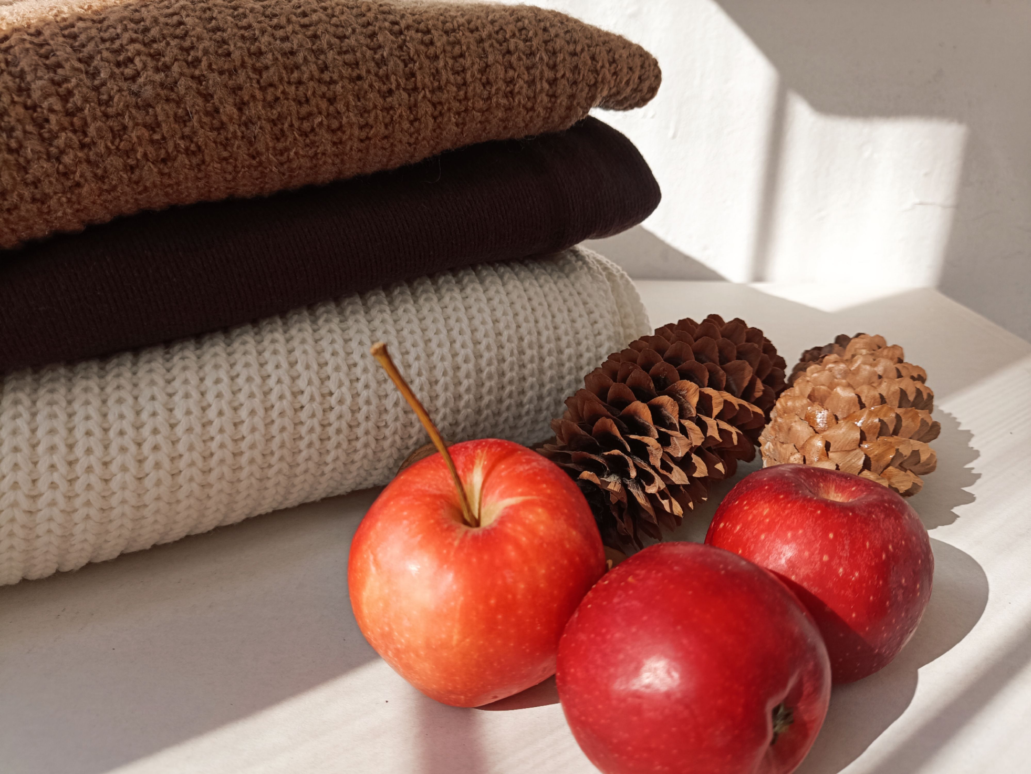 Stacked sweaters with apples and pinecones in warm autumn light.