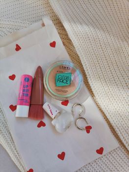 Cosmetics and accessories arranged on a cozy fabric surface with a heart-patterned bag.
