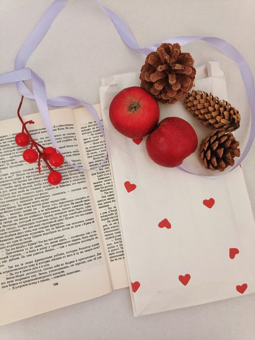 Free A flat lay of an open book, apples, pine cones, and a heart-patterned bag. Stock Photo