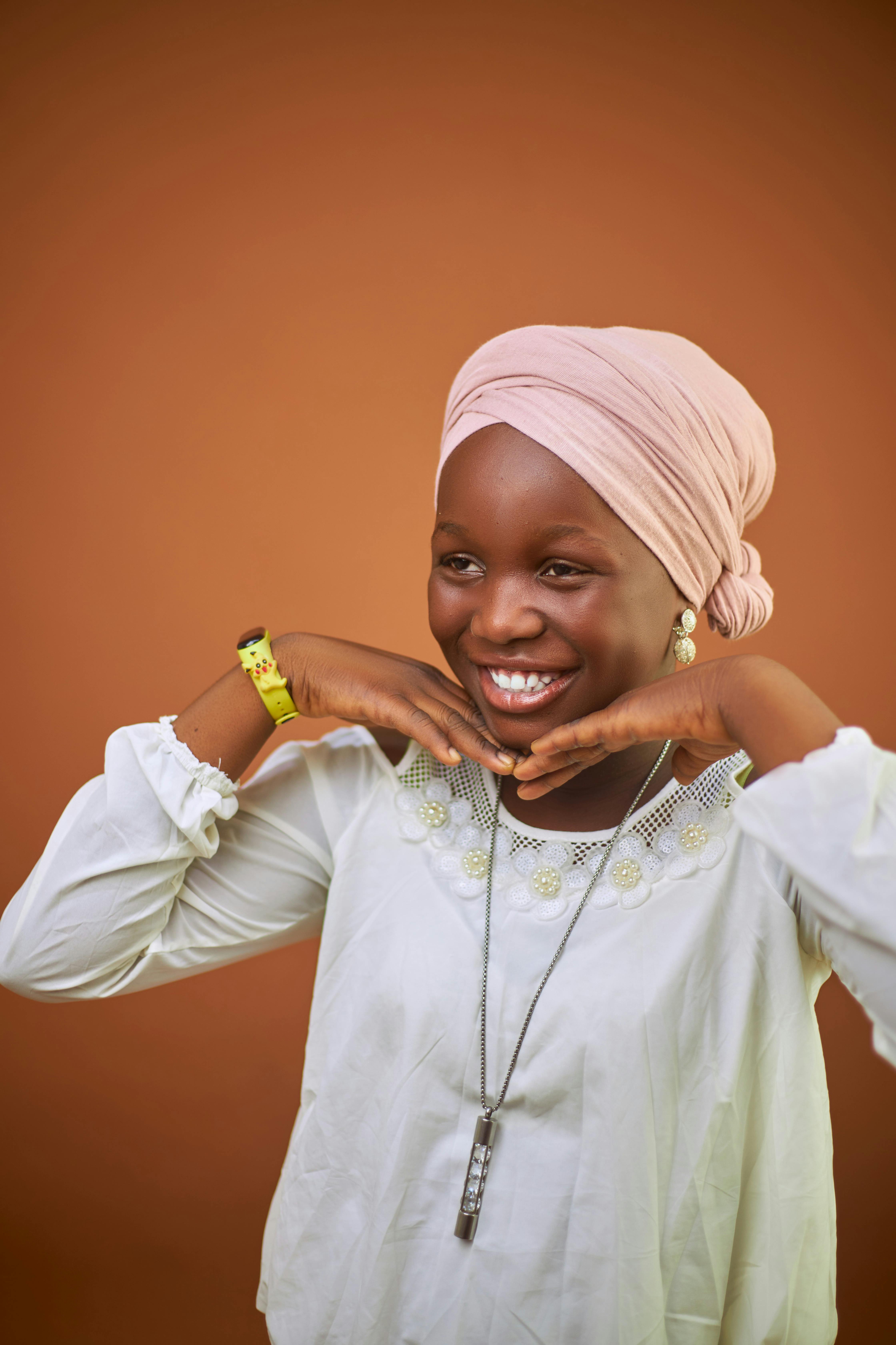 Smiling young woman posing playfully in traditional attire with hijab.
