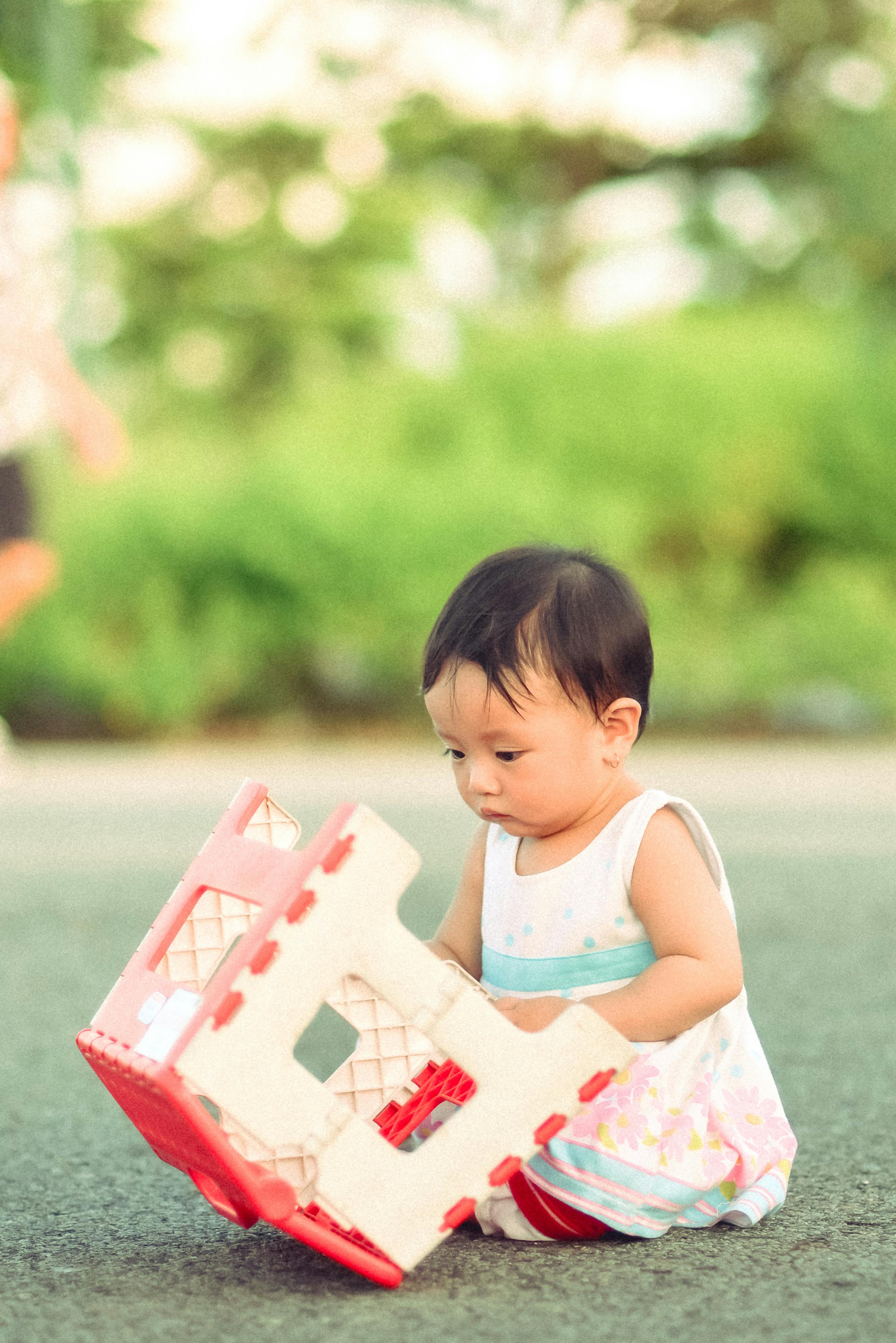 Cute baby playing with a toy house outdoors, enjoying a sunny day.
