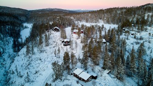 Free Serene aerial view of snow-covered cabins in Krøderen, Norway at sunset, amidst a winter pine forest. Stock Photo