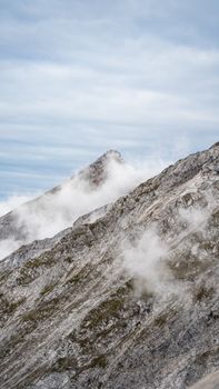 Stunning view of rocky alpine mountains with mist and clouds enveloping the peaks.