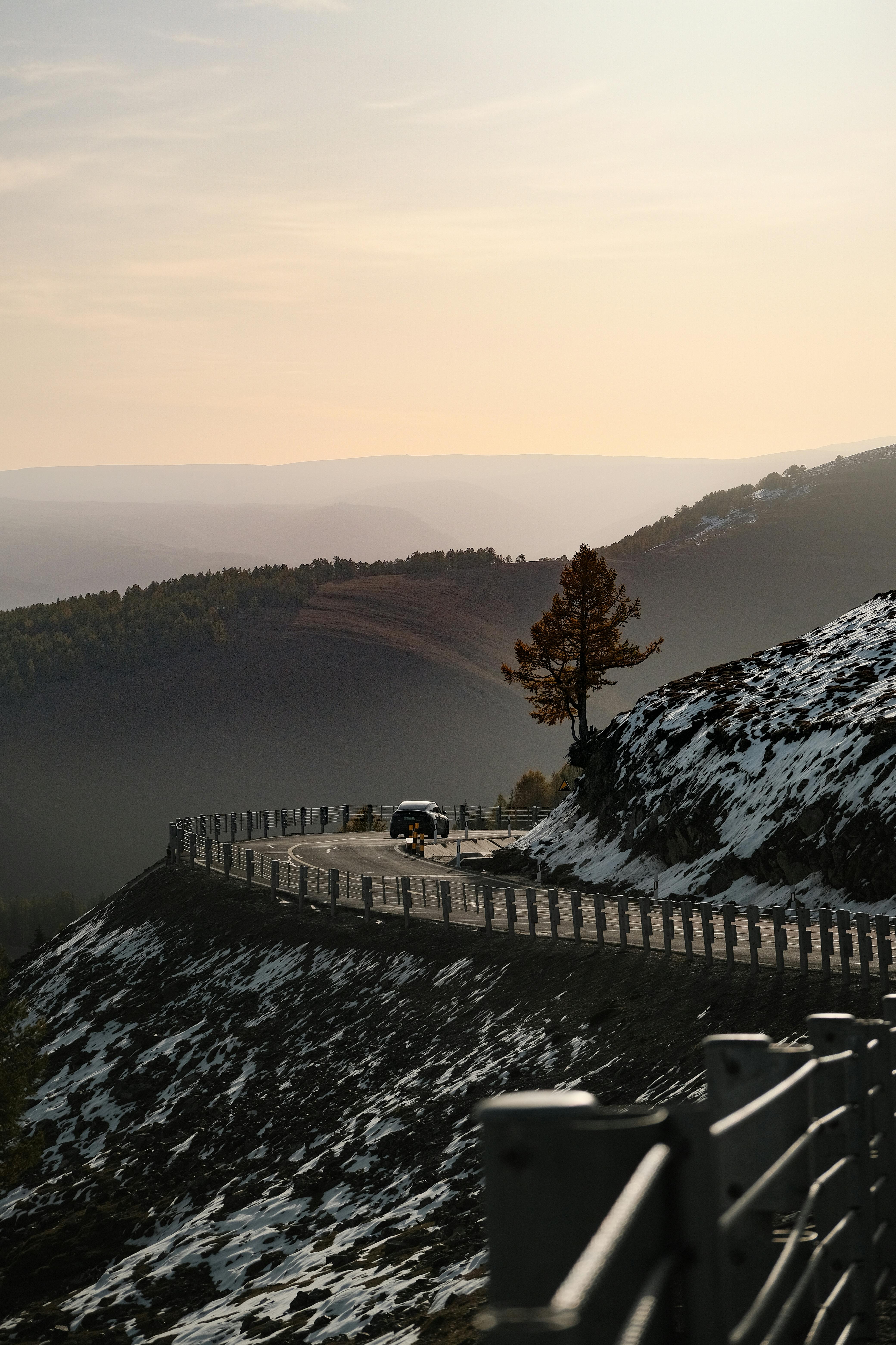 A car drives along a snowy mountain road during sunset, offering a dramatic scenic view.