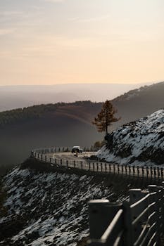 A car drives along a snowy mountain road during sunset, offering a dramatic scenic view.