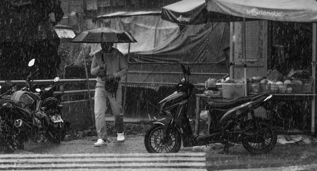 A person with an umbrella walks through heavy rain in Baguio City street market setting.