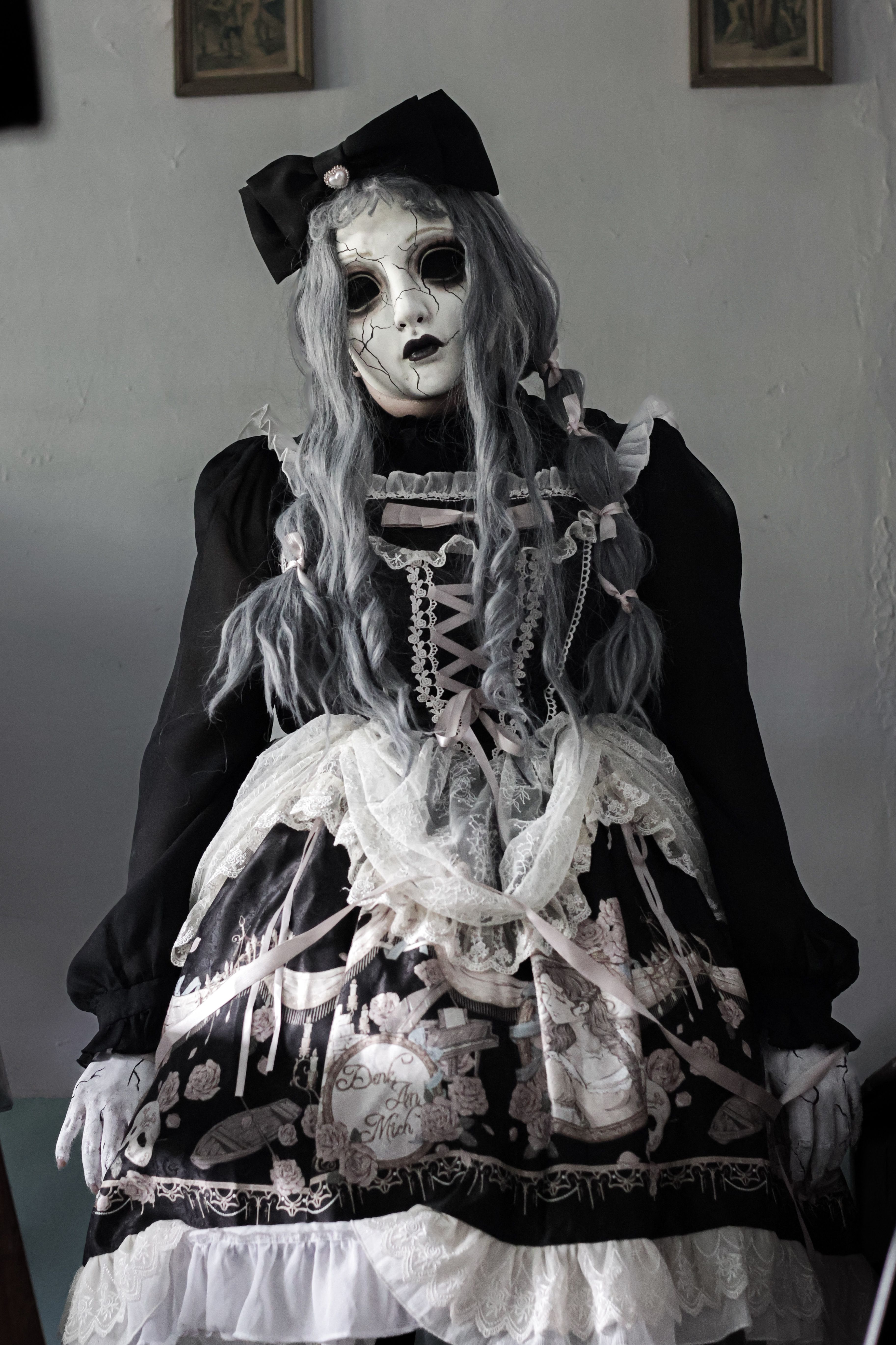 Eerie gothic lolita doll in lace dress and white mask indoors, spooky atmosphere.