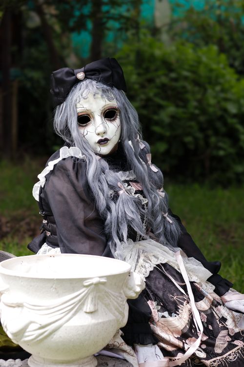 Free A mysterious doll in Gothic attire sits in a garden, exuding an eerie charm. Stock Photo